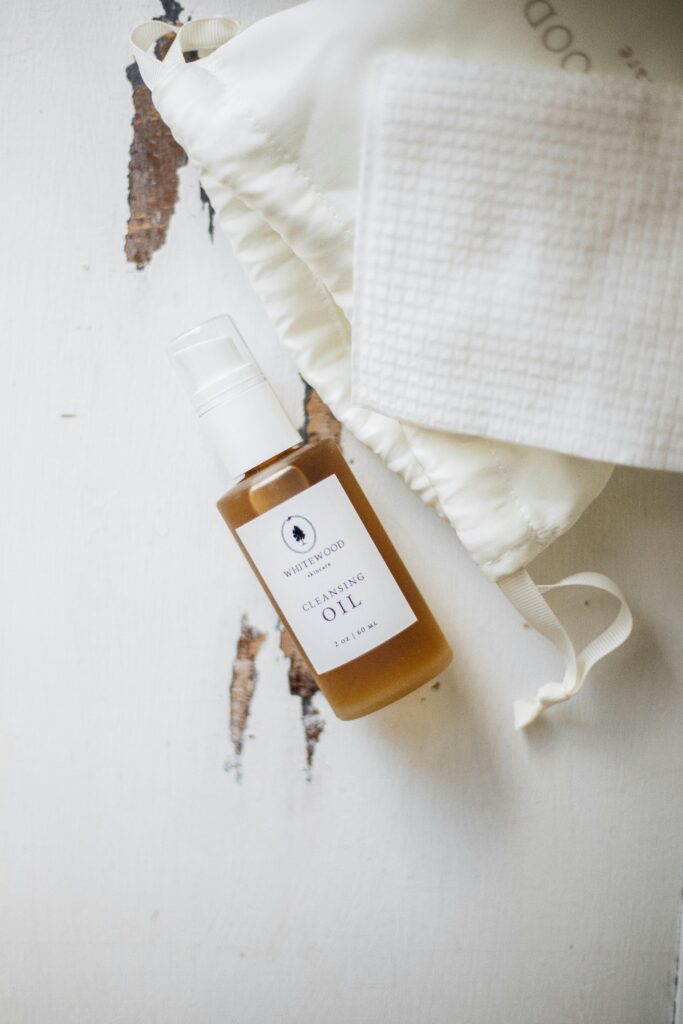 Flat lay of cleansing oil bottle with cloth bag on rustic surface. Perfect for beauty and wellness imagery.